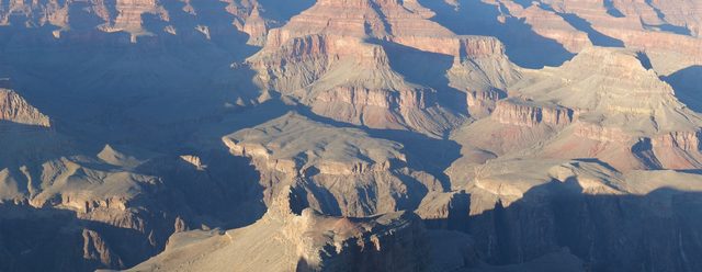 Layered red and tan cliffs of the Grand Canyon dropping away under soft morning light