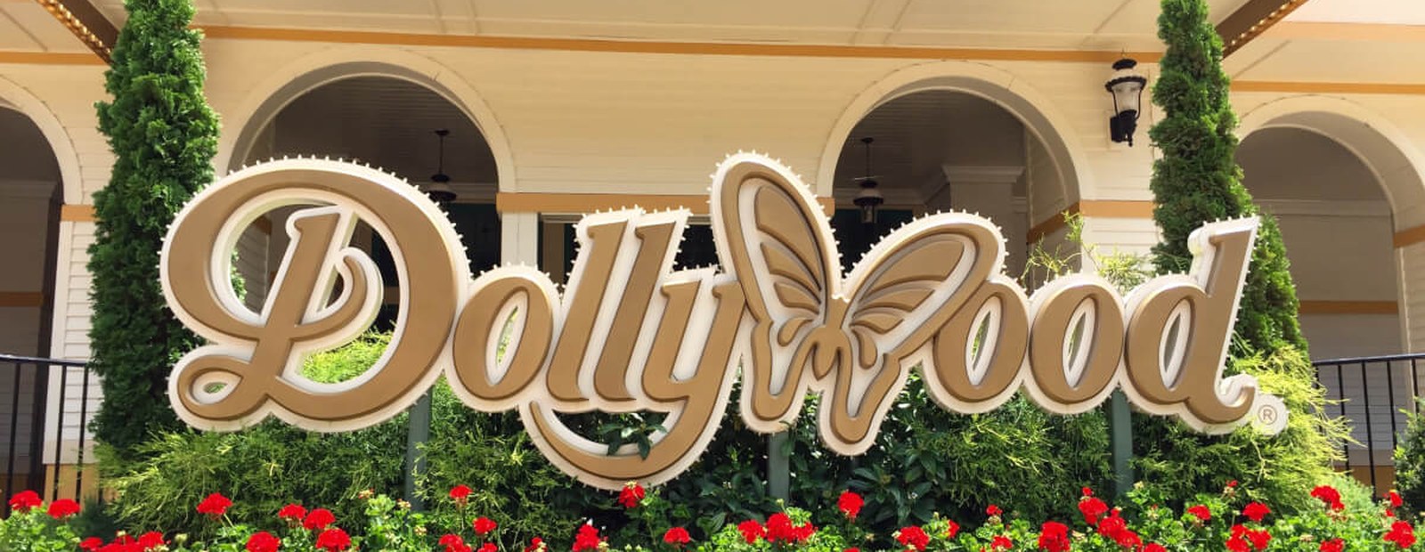 The wooden Dollywood entrance sign surrounded by cypress trees and red flowers