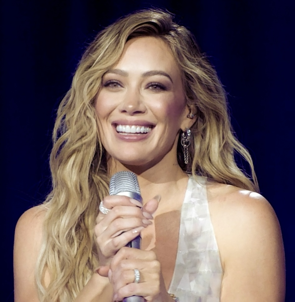 Hilary Duff smiling on stage with a microphone