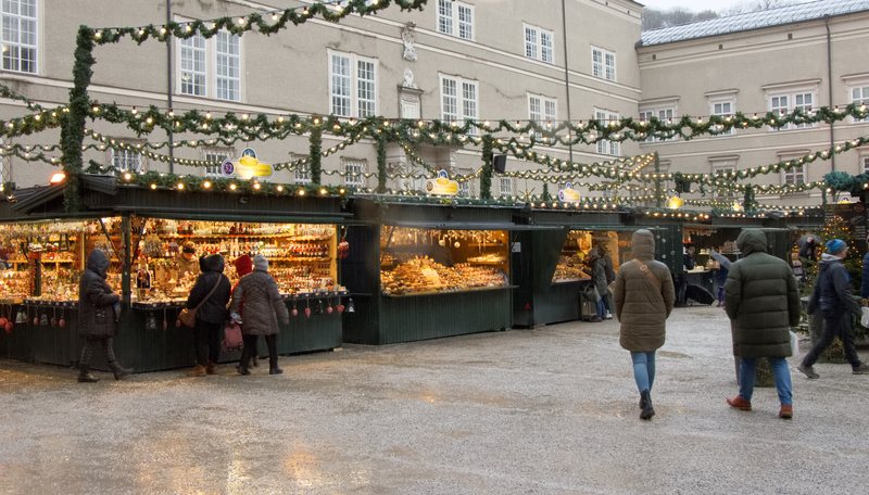 Lit wooden Christmas market stalls strung with garlands in an old-town square.