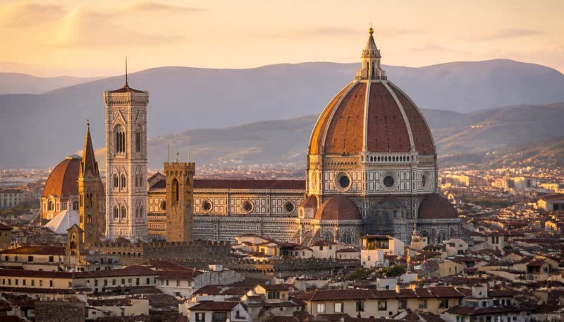 The terracotta dome of Florence Cathedral rising above rooftops with hills behind