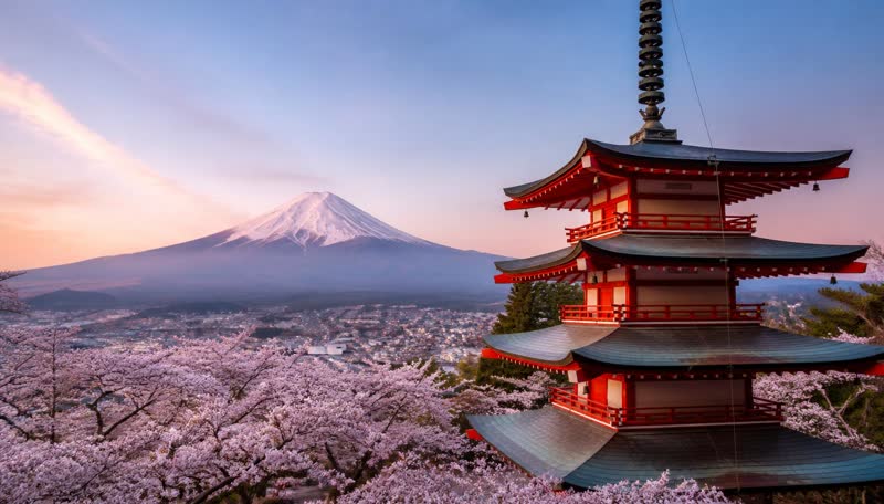 A red five-story pagoda framed by cherry blossom with snow-capped Mount Fuji behind