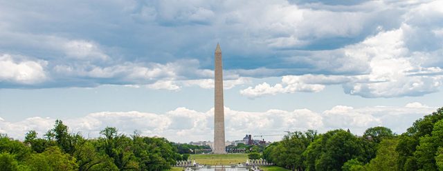 The Washington Monument seen across green lawn and trees under big cumulus clouds