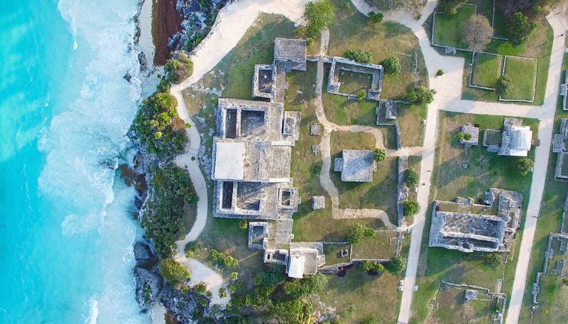 Aerial view of the Tulum ruins on the cliff above turquoise Caribbean water.