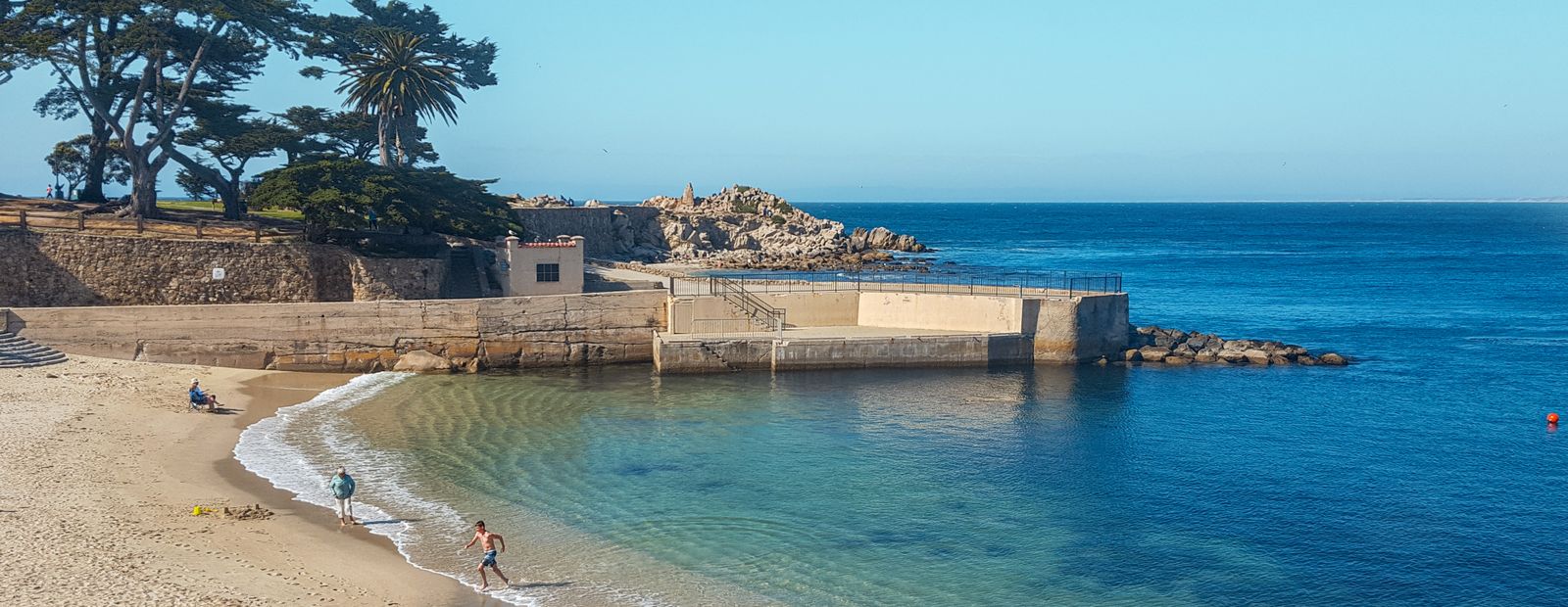 A calm turquoise cove with a sheltered swimming beach and stone breakwater