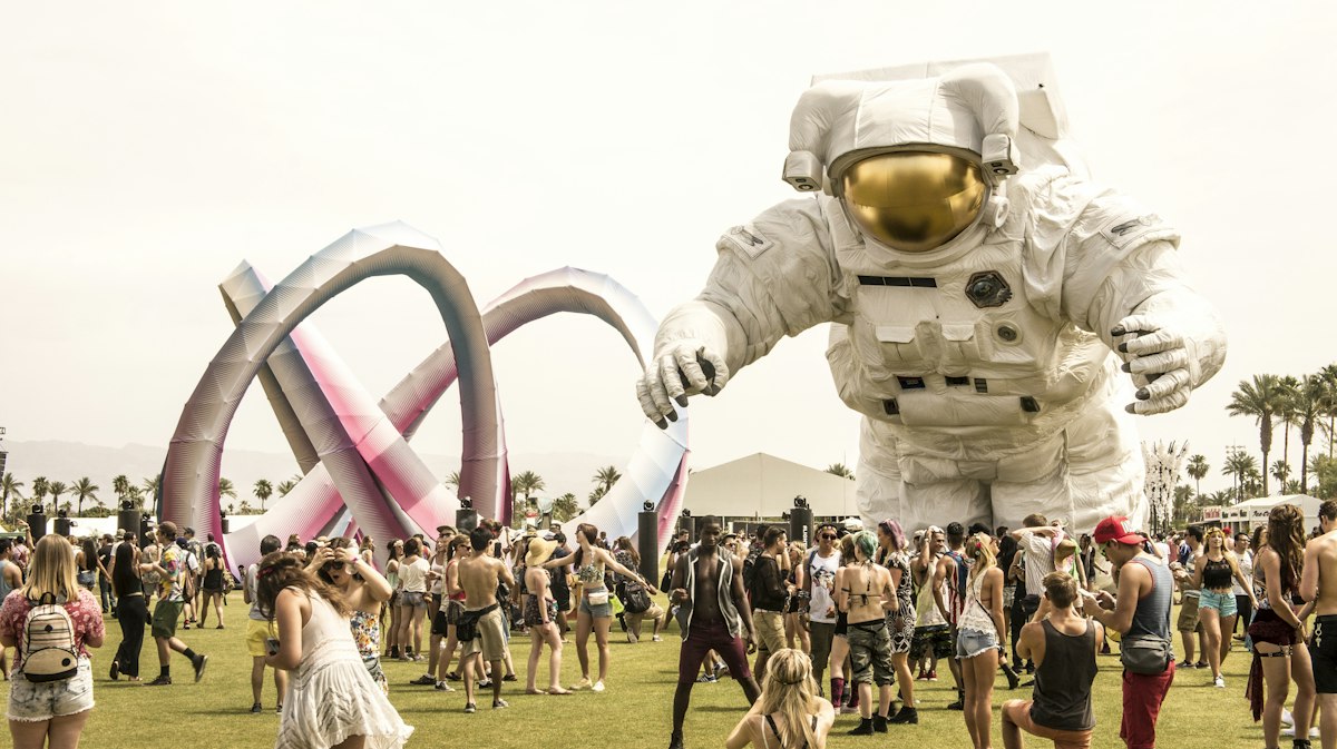 Festival crowd on the grass beside a giant astronaut sculpture